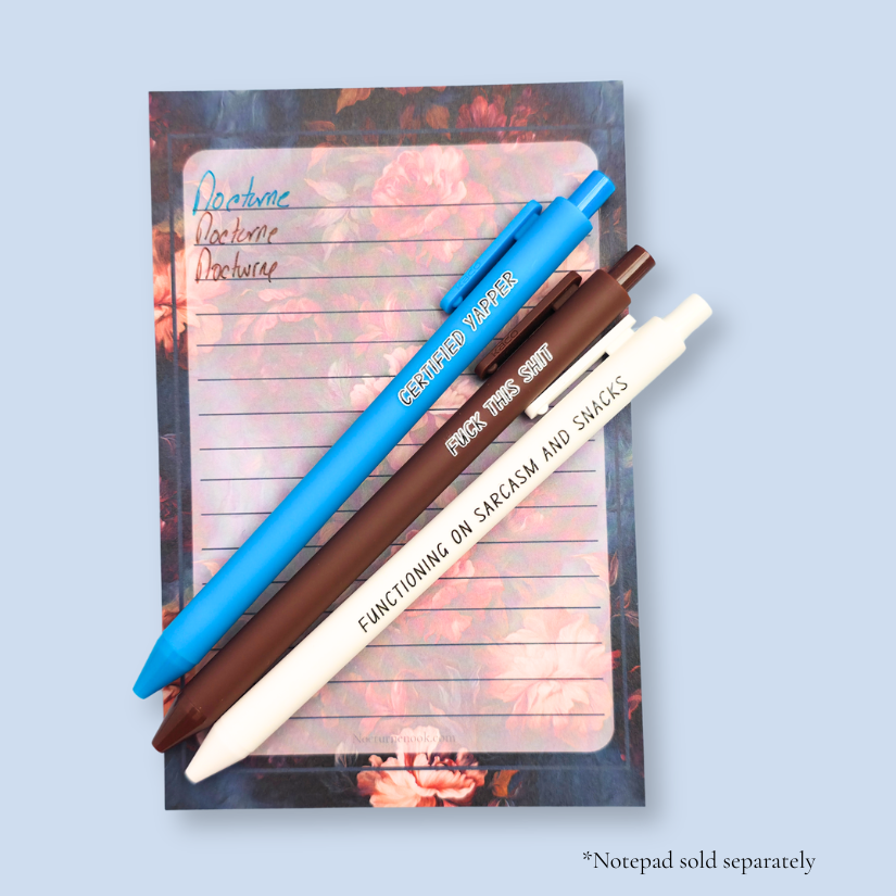 Three pens with sayings on them. "certified yapper" (bright blue pen), "Functioning on sarcasm and snacks" (white pen), "fuck this shit" (brown pen).