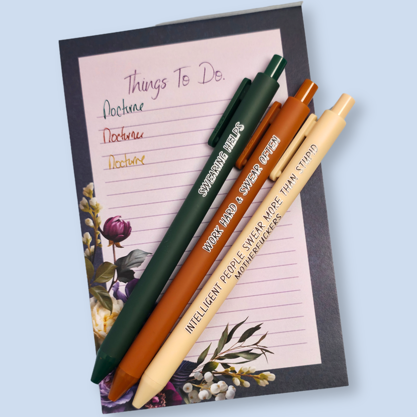 Three pens with sayings on them. "Swearing Helps"(forest green pen), "Work Hard & Swear often" (sienna pen), "Intelligent people swear more than stupid motherfuckers" ( linen pen). They are on top of a notepad, with a sample of the ink. Ink matches the color of the pen. Notepad not included