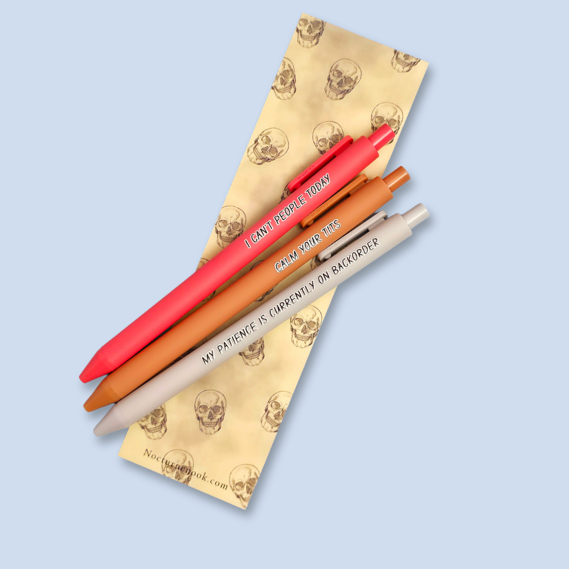 Three pens on a yellow bookmark with skull designs on a light blue background