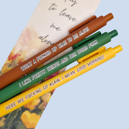 Three pens with sayings on them. "here we fucking go again. I mean, Good morning!"(bright yellow pen), "What a fucked up time to be alive" (sienna pen), "I like pretty things and the word fuck" ( green pen)
