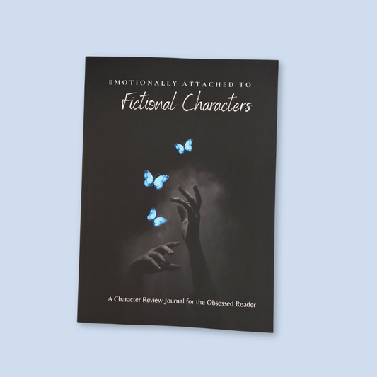 A dark journal titled 'Emotionally Attached to Fictional Characters' with a cover showing blue butterflies and raised hands, photographed against a light blue background.